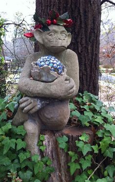 a stone statue holding a ball in its arms next to a tree and ivy covered ground