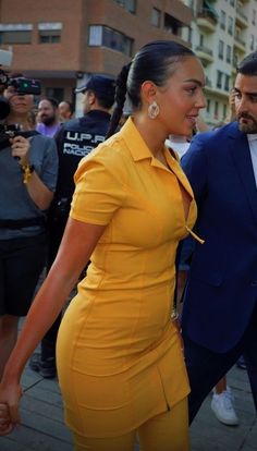 a woman in a yellow dress and a man in a blue suit are walking down the street