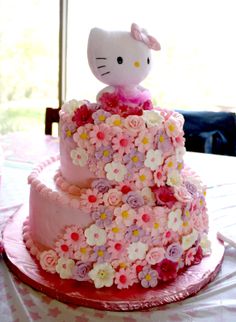 a hello kitty cake is decorated with pink and white flowers on a tablecloth covered table