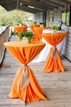 two tables with orange cloth draped over them on a wooden deck at an outdoor event