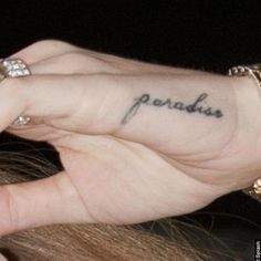 a woman with a small tattoo on her left hand and the word paradise written in cursive font