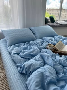 an unmade bed with a book on it in front of a window overlooking a city