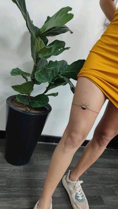 a woman in yellow dress standing next to a potted plant and wearing white tennis shoes