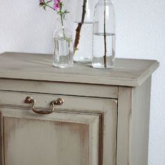 two vases with flowers are sitting on top of an old dresser drawer, one is empty and the other has water in it