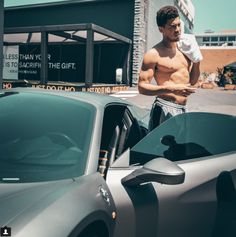 a shirtless man standing next to a sports car