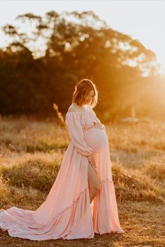 a pregnant woman in a pink gown standing on the grass with her back to the camera