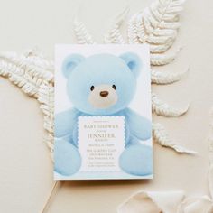 a blue teddy bear is on the front of a baby shower card with fern leaves around it