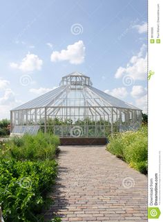 a brick walkway leading to a large glasshouse in the middle of some plants and flowers