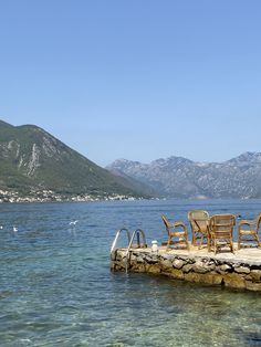 some chairs are sitting on a dock in the middle of water with mountains in the background