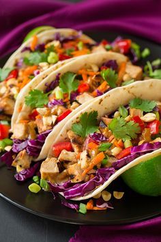 three tacos on a black plate with limes and cilantro garnish