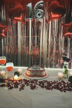 a table topped with a cake covered in frosting and red balloons next to candles