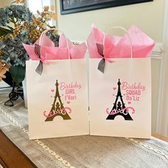 two bags with pink bows are sitting on a table in front of a flower vase