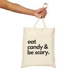 a person holding a tote bag with the words eat candy and be scary on it