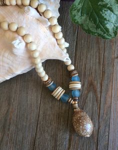 a wooden beaded necklace with shells and seashells on a wood table next to a plant