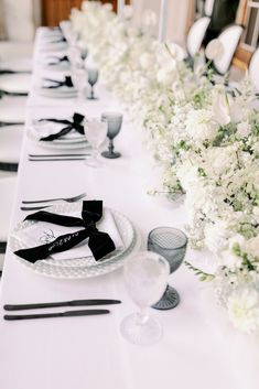 a long table is set with black and white place settings, silverware, and flowers