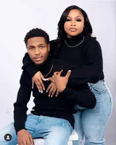 a man and woman sitting next to each other on a white surface with their arms around one another