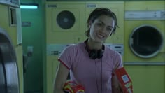 a woman with headphones is holding some food in front of washers and dryers