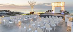 an outdoor event setup with white chairs and candles on the floor, overlooking the ocean