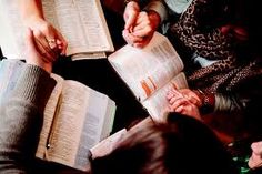 two people sitting at a table with open books in front of them, one holding the other's hand