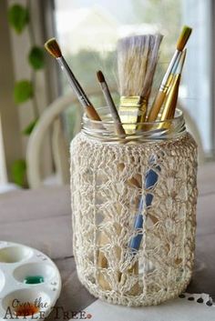 a mason jar filled with paint brushes and crocheted yarn on top of a table