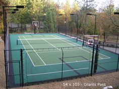 an outdoor tennis court surrounded by trees and basketball hoops in the middle of it