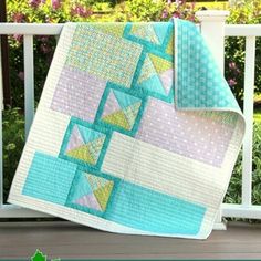 a quilted blanket sitting on top of a wooden bench next to a white fence