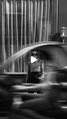 a black and white photo of a woman standing in front of a window with cars passing by