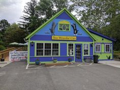 a blue and green building sitting in the middle of a parking lot next to trees