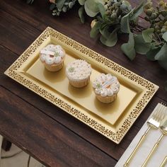 three cupcakes sitting on a yellow plate next to silverware and greenery