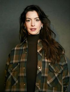 a woman with long dark hair wearing a green plaid jacket and black turtle neck sweater