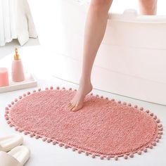 a person standing on a pink rug in a bath room next to a white tub