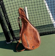 a brown leather guitar case sitting on top of a tennis court next to a net