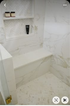 a bathroom with white marble walls and flooring next to a shelf on the wall