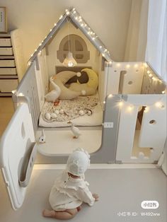 a baby sitting on the floor in front of a doll house with lights and decorations