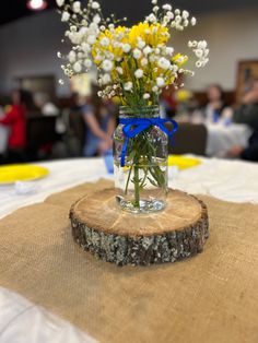 a vase filled with yellow and white flowers on top of a wooden slice at a table