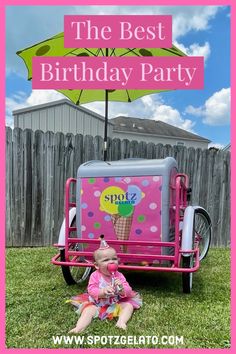 a baby sitting on the grass in front of a pink ice cream cart with an umbrella