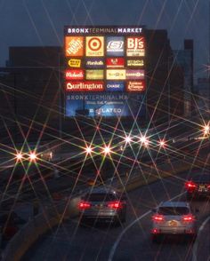 cars driving down the road at night with lights shining on it's screen and buildings in the background