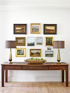 a wooden table sitting in front of a wall filled with pictures and lamps on top of it