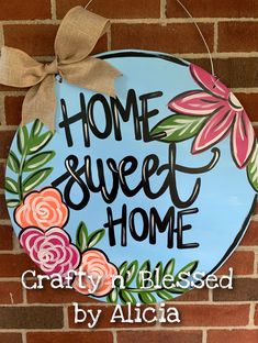 a sign that says home sweet home with flowers and leaves painted on the side of a brick wall