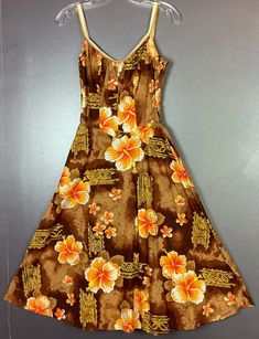 This vintage 1960s Hawaiian style sundress has a bright orange, yellow and brown floral print. The neckline is a deep "U" with gathers for a flattering bust. There is also a nice deep "U" cut in the back. The straps connect at each side in the back and have sliding hardware to make the straps adjustable. The straps are a continuous white band with a smaller gold band underneath it. There is a tiny little diamond point at the center waistline, very flattering. Elastic is at the sides and continues around to the back. There is still stretch in the elastic for now. The dress skirt is flat in the front but more gathered in the back.  Someone has thankfully cut out the hard structured part of the bra part of this dress which has probably made it more comfortable. The elastic strap that goes aro Retro Brown V-neck Dress, Vintage Orange Floral Print Dress, Vintage Brown Floral Print Dress, 1970s Style Orange Summer Dress, Vacation Brown Floral Print Sundress, Vintage V-neck Sundress, Vintage Floral Print Sundress For The Beach, Retro Orange Dress For Beach, Retro Orange Beach Dress