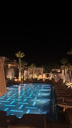 an outdoor swimming pool at night with lounge chairs and umbrellas in the foreground