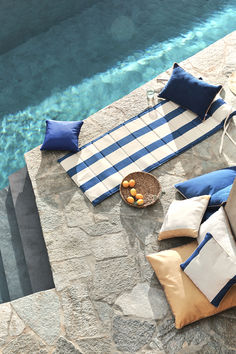 an outdoor patio with blue and white striped cushions next to a swimming pool filled with water