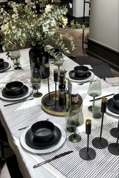 the table is set with black and white plates, silverware, and flowers in vases