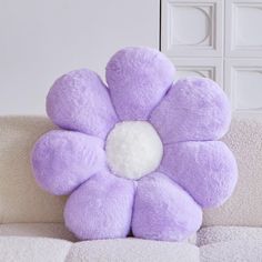 a purple flower shaped pillow sitting on top of a white couch next to a wall