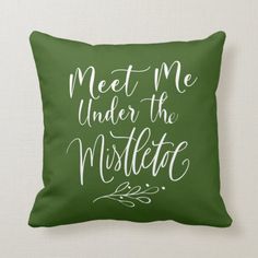 a green pillow with the words meet me under the mistle