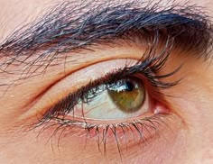 an extreme close up shot of someone's eye with long black hair on it