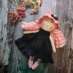 a doll with pink hair and black dress laying on wooden floor next to dried flowers