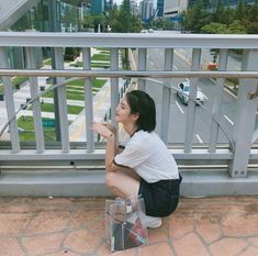 a woman squatting on the ground next to a railing