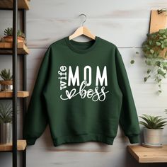 "Empowerment meets style with our Wife, Boss Mom sweatshirts! 💪 Show the world that you can do it all with grace and flair. Whether you're tackling work projects or nurturing your family, these sweatshirts are a reminder of your strength and determination. Own your roles with confidence and fashion! .: Made using 100% ethically grown US cotton.  We create designs made with love and we strive to make your shopping experience great.  GILDAN SWEATSHIRT .: Made using 100% ethically grown US cotton. Wife Sweatshirt, Boss Mom, Stylish Mom, Gildan Sweatshirts, Mom Tees