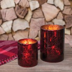 two red glass candles sitting next to each other on top of a wooden table with logs in the background